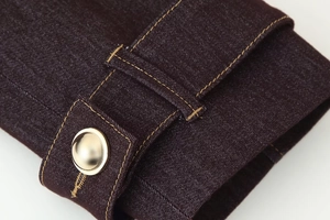 Détail macro d'une manche en denim bordeaux avec surpiqûres contrastées et boutons dorés
