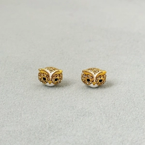 Macro detail of golden owl earrings with white enamel coating and sparkling rhinestones