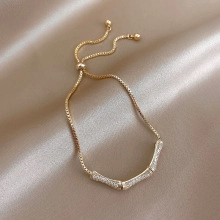 Detail of gold box chain bracelet with sparkling zircon bar on champagne silk background