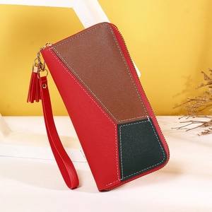 Détail d'une pochette en cuir tricolore avec pompon et dragonne sur fond de tons chauds