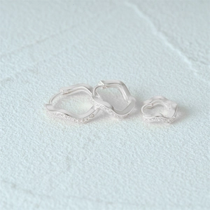 Detailed view of three different sizes of silver irregular wavy hoop earrings with crystals