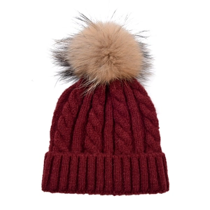 Dettaglio del berretto in maglia a trecce bordeaux con grande pompon in ecopelliccia