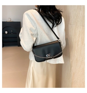 Detail shot of a black leather shoulder bag with silver chain and metal buckle on a model
