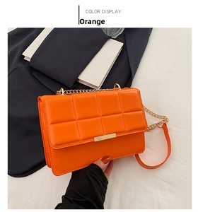 Detail of orange quilted crossbody bag with gold metal clasp and chain strap