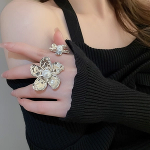 Detailed view of silver flower rings with white pearls on a model wearing black knitwear