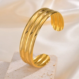 Macro view of gold multi-layer ribbed cuff bracelet on a white stone and silk surface