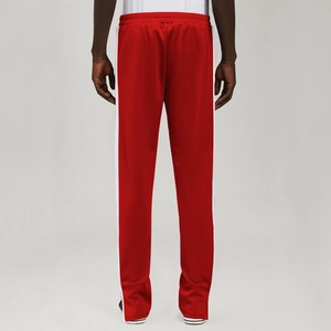 Detail of red athletic sweatpants featuring classic double white side stripes on the leg