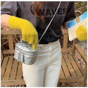 Close-up of yellow knitted gloves holding a silver quilted chain bag in outdoor setting
