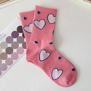 Dettaglio calzini di cotone rosa con motivi a cuore bianchi e blu su un tavolo bianco