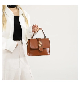 Detail of a brown vintage square bag with a golden double ring buckle held by a model