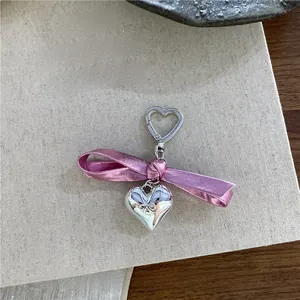 Detailed close-up of a silver heart charm with a metallic pink bow on a heart-shaped clip