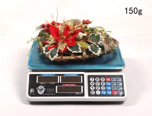 Close-up of a 150g Christmas heart wreath with red poinsettia on a digital weight scale