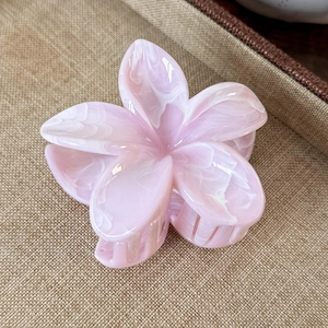 Detailed macro view of a pink marble acrylic plumeria flower claw clip on brown fabric