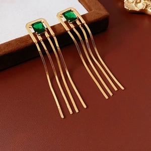Close-up of golden tassel earrings featuring square green gemstones and metal fringe
