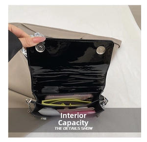 Internal storage view of black glossy patent crossbody bag with smartphone and sunglasses