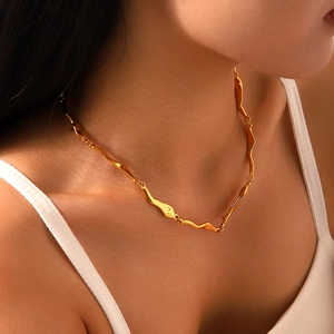 Detail shot of irregular wave-shaped gold necklace on a model showing smooth metallic texture