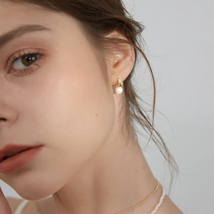 Elegant gold hoop earrings with white pearl pendants worn by a model on grey background