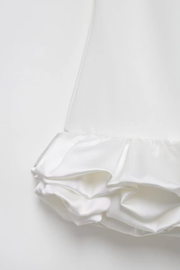 Macro detail of white satin dress featuring layered ruffle hem and glossy fabric texture
