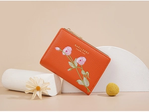 Detail of orange short wallet with floral embroidery and gold zipper on a beige background
