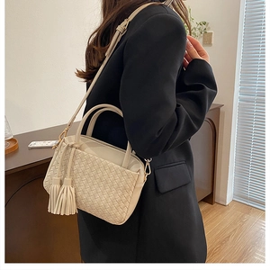 Close-up of beige woven texture with leather tassels and gold hardware on shoulder bag