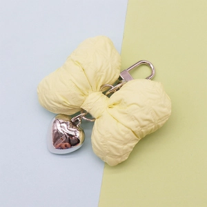 Yellow quilted fabric bow keychain with silver heart pendant on a soft pastel background