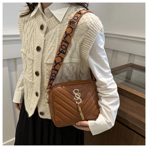 Detail of brown crossbody bag with V-quilt pattern, metal logo, and wide woven strap