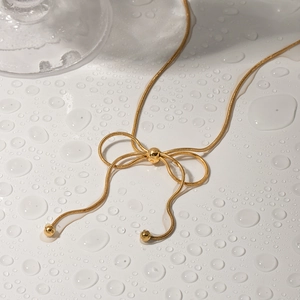 Detail of golden snake chain necklace featuring a butterfly pendant over water droplets