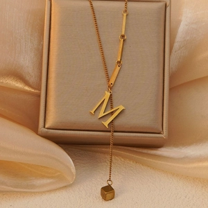 Detailopname van gouden halsketting met letter M en kubuskwastje op satijnen stof