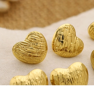 Macro detail of gold 18K plated heart earrings with woven texture on linen background