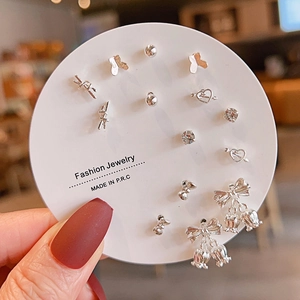 Close-up of a silver earring set with butterfly and heart studs held in hand