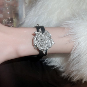 Nahaufnahme eines funkelnden Strass-Rosenanhängers an einem schwarzen Lederarmband