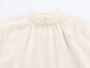 Detailed view of women's pleated high collar and back button on ivory chiffon top