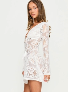 Detail of white crochet lace dress featuring long sleeves and tassel drawstring neckline