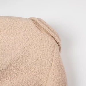 Detail shot of beige boucle wool coat shoulder showing high-quality textured fabric