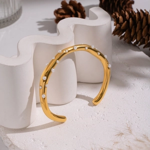 Close-up of gold plated pearl open bangle displayed on a minimalist white wavy stone stand