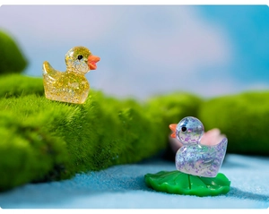 Miniature glittering resin ducks in yellow and purple set on moss and lotus leaf