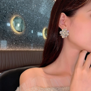 Detailed view of luxury gold flower earrings with sparkling crystals worn by a model