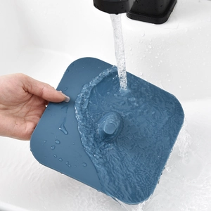 Square blue silicone drain cover being rinsed under tap water in a white sink basin