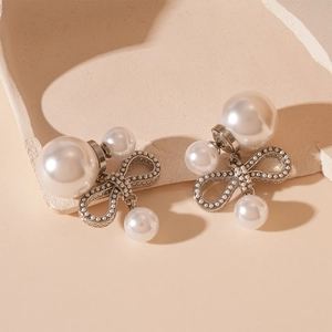 Detail shot of elegant silver bow earrings with double pearls on beige stone surface