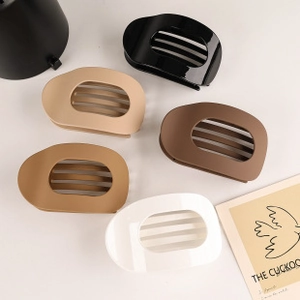 Flat lay of five matte oval hair claw clips in black, beige, white, and brown shades