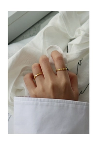 Close-up of dual gold S925 silver beaded rings worn by a model on a soft fabric background