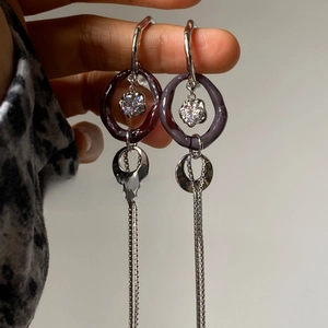Macro detail of silver drop earrings featuring purple resin hoops and long chain tassels
