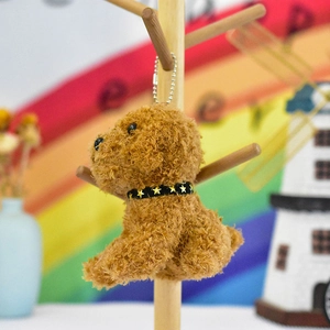 Side view of a cute brown teddy dog plush keychain hanging on a wooden stand