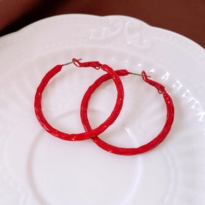 Detail of red hammered metal hoop earrings displayed on a white textured ceramic dish