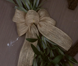 Detail of burlap bow with artificial green olive leaves for festive door wreath decor