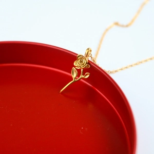 Classic golden rose pendant necklace in stainless steel displayed on a red edge