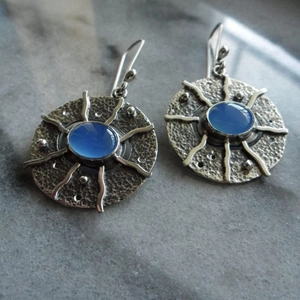 Retro geometric sunburst silver earrings with blue gemstone on marble surface