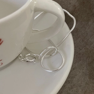 Minimalist S925 sterling silver snake chain bracelet draped on a white ceramic teacup