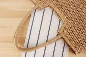 Detailed top view of a woven straw shoulder bag on a blue striped napkin and wood background