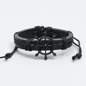 Detailed view of black woven leather bracelet with a vintage metal rudder charm